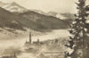 Schwarz-weiße historische Fotografie von Davos, aufgenommen um 1925. Der Blick zeigt eine morgendliche Szene: Lichtnebel liegt über den Bergen und Tälern, während die ersten Sonnenstrahlen die Gipfel erhellen. Die Stadt Davos ist in der Tiefe sichtbar, umgeben von einer majestätischen Alpenlandschaft.