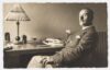 Thomas Mann, Brustbild, Profil nach links, Kopf leicht nach vorne gewendet, im Stuhl zurückgelehnt schräg vor dem Schreibtisch sitzend, Zigarette in der linken Hand.